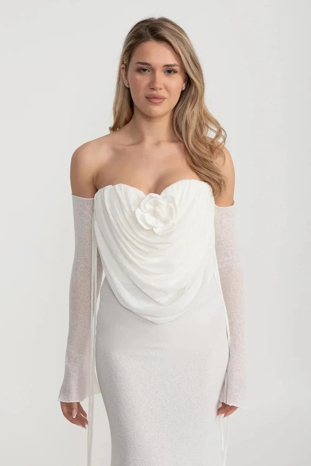 An elegant, flowing white dress with long sleeves, a draped bodice, and a rose embellishment in the center.