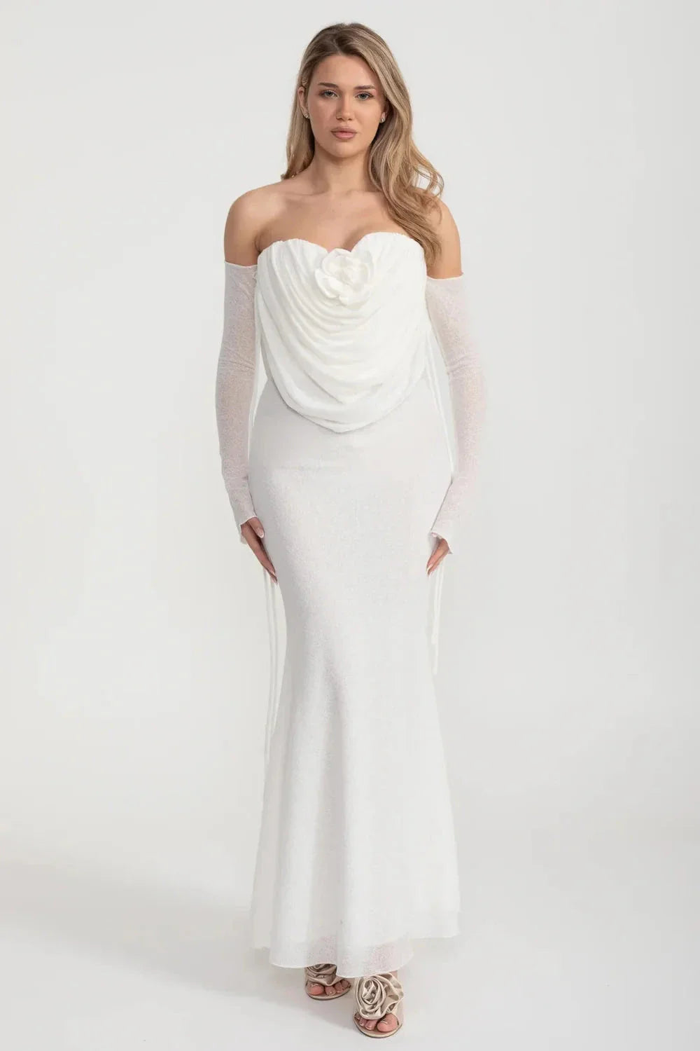 An elegant, flowing white dress with long sleeves, a draped bodice, and a rose embellishment in the center.