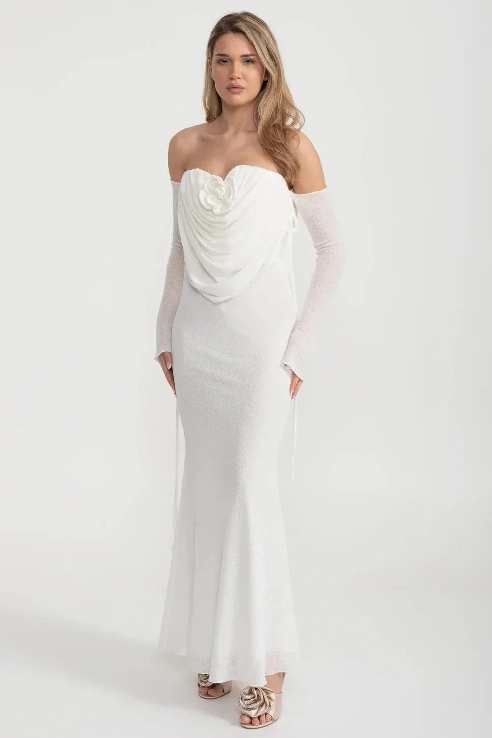 An elegant, flowing white dress with long sleeves, a draped bodice, and a rose embellishment in the center.