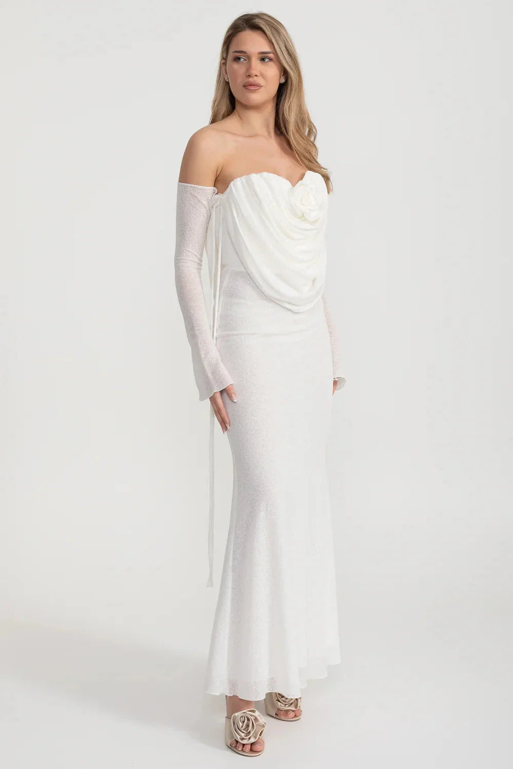 An elegant, flowing white dress with long sleeves, a draped bodice, and a rose embellishment in the center.